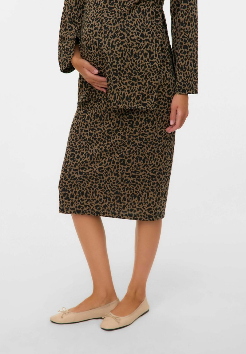 La robe de maternité présente un motif léopard marron et noir, longueur genou, avec des manches longues. Associée à des ballerines beige clair.