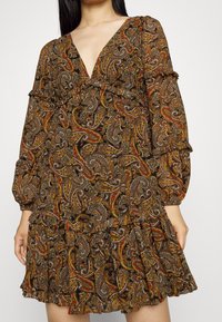 Vestido marrón de paisley con un escote en V profundo, acentos con volantes y largas mangas abullonadas. Presenta un dobladillo en capas y acampanado, con vibrantes patrones multicolores.
