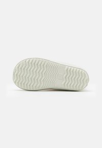 Semelle de sneaker blanche avec un motif en chevrons, forme de bout arrondi et texture lisse. Présente un petit logo au centre.