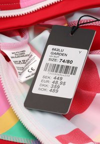 UV-Anzug mit mehrfarbigen Mustern in Rot-, Pink- und Grüntönen. Das Etikett zeigt die Größe 74/80 und die Preise in verschiedenen Währungen.