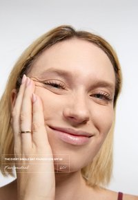 Produit de fond de teint beige neutre appliqué sur la peau, avec un gros plan sur le visage d'une personne, mettant en avant une peau claire, des cheveux blonds et une texture de peau saine.