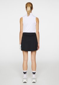 Vit ärmlös polo med krage, i kombination med en svart kjol. Modellen bär vita och svarta randiga strumpor samt ljusa skor.