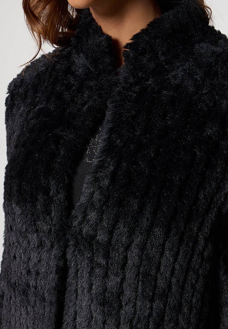 Fekete műszőrme kabát texturált mintázattal, magas gallérral és nyitott elülső kialakítással. Puha, plüss anyag sűrű megjelenéssel.