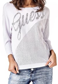 Pull en maille violet clair avec une texture en maille et un logo "Guess" argenté. Il présente des manches longues et une coupe décontractée, associé à un jean en denim.