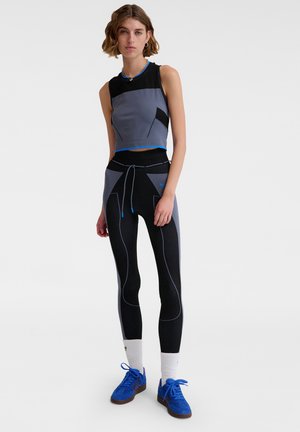 Trainingsset bestaande uit een grijs en zwart mouwloos crop top met blauwe accenten, gecombineerd met aansluitende zwarte leggings met textuurelementen.