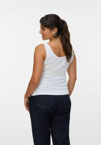 Débardeur blanc en tissu doux, avec de larges bretelles et un col rond, associé à un pantalon en denim bleu foncé.