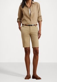 Khaki-shorts med en skräddarsydd passform, i kombination med en beige linneskjorta. Ett brunt läderbälte och loafers fulländar outfiten. Samt en jämn textur och avslappnad design.