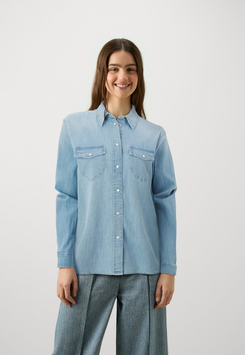 Svijetloplava traper košulja s dugim rukavima, dugmadi sprijeda, dva džepa na prsima i dugmadima kao ukras. Ima klasičan ovratnik i mekanu teksturu.