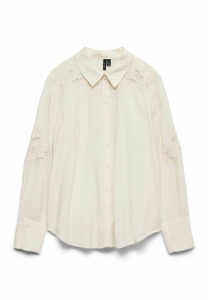 Chemise crème boutonnée, avec un col et des détails en dentelle sur les épaules. Manches longues avec poignets boutonnés, confectionnée dans un tissu léger.