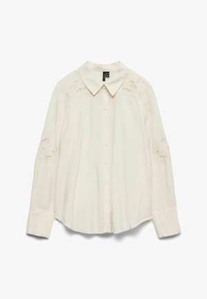 Kreemikas nööbitav särk, millel on krae ja õlgadel pitsdetailid. Pikad varrukad nööbitavate mansettidega, tehtud kergest kangast.