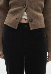 Brown wool cardigan with two buttons, paired with black corduroy pants featuring front pockets and a slight flare at the bottom.