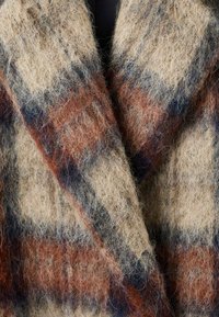 Abrigo de mezcla de lana con una textura suave y difusa, con un patrón de cuadros en beige, óxido y azul marino. Destaca por su diseño de cuello y solapa de gran tamaño.