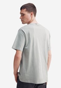 T-shirt in cotone grigio chiaro con maniche corte, scollo rotondo e vestibilità rilassata, mostra una trama minima e nessun motivo o accento visibile.