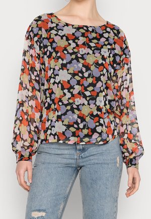 Czarna, przezroczysta bluzka z długim rękawem z wielokolorowym kwiatowym nadrukiem, zestawiona z jasnoniebieskimi, przetartymi dżinsami.