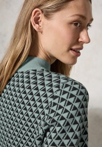 Gebreide trui met een geometrisch patroon in zwart en teal driehoekjes, voorzien van een geribde kraag. De textuur lijkt zacht en is geschikt voor casual dragen.