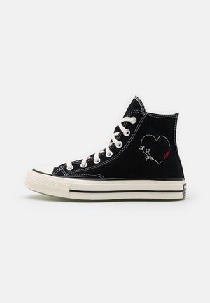 Schwarze High-Top-Sneaker aus Canvas mit weißen Ösen, kontrastierender Naht und einem auf der Außenseite in Weiß und Rot gestickten Herzmotiv.