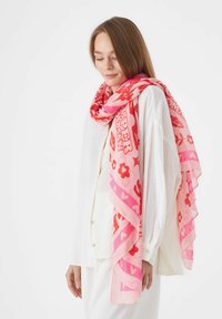 Écharpe à motifs roses et rouges avec des designs floraux et le texte "SUPER WOMAN", fabriquée en tissu léger, tombant lâchement autour du cou d'un modèle.