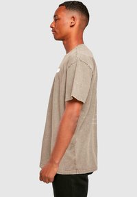 Grå, avslappet passform t-skjorte med korte ermer, med rund hals og slitt tekstur, vist på en mannlig modell i profil.
