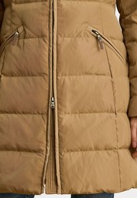 Barna puffkabát, elöl cipzárral, vízszintes steppeléses mintával, két oldalsó zsebbel és sima felülettel. Melegségre és kényelemre tervezve.