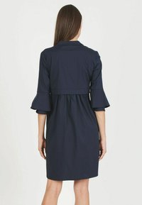 Abito blu navy con top aderente, maniche a tre quarti svasate e gonna arricciata. Tessuto morbido con un design semplice.