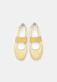 Scarpe flat gialle in pelle con design in rete, dotate di una fascia elastica sul collo del piede e una suola bianca. Superficie liscia e forma arrotondata.