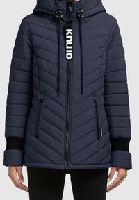 Granatowa kurtka puchowa z wzorem w zygzak, podszewkowym kapturem, przednim zamkiem błyskawicznym i czarnymi dzianinowymi mankietami. Posiada wyraźne logo marki na zamku.