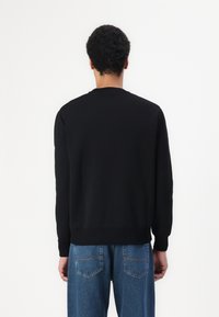 Pulover negru cu mânecă lungă, guler rotund și manșete striate, asortat cu blugi din denim deschis la culoare. Are o textură netedă.