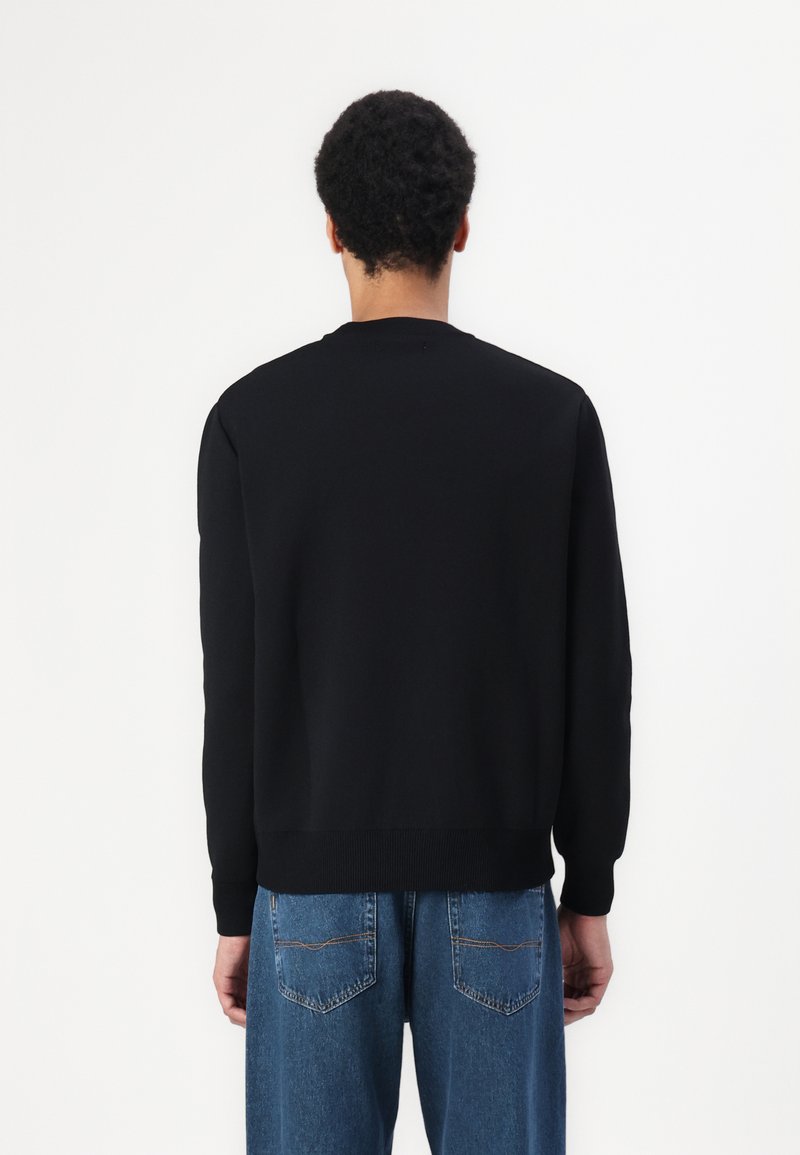 Maglione nero a maniche lunghe con scollatura rotonda e polsini a costine, abbinato a jeans in denim azzurri. Presenta una texture liscia.