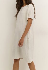 Robe droite en lin beige clair avec manches courtes, encolure ronde, poches latérales et coupe ample, offrant un look décontracté.