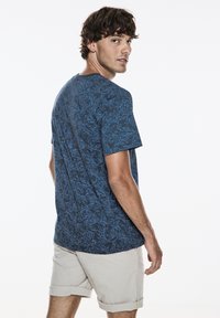 Námořnické modré tričko s krátkým rukávem, modrý květinový vzor, kulatý výstřih a uvolněný střih. Model má na sobě světle béžové šortky.