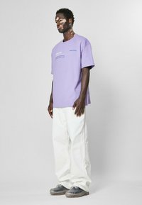 Lavender t-shirt with short sleeves, printed text on the front; paired with loose-fitting white pants and gray shoes with clear soles.