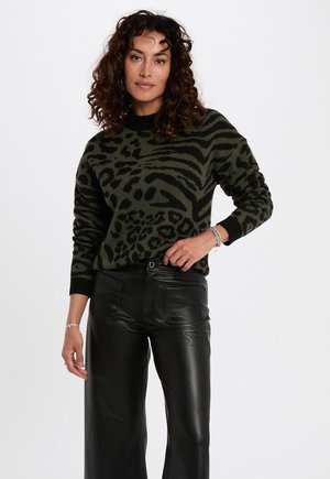 Pull vert avec un motif animalier noir, décolleté rond, poignets côtelés, associé à un pantalon en cuir noir. Coupe texturée et décontractée.