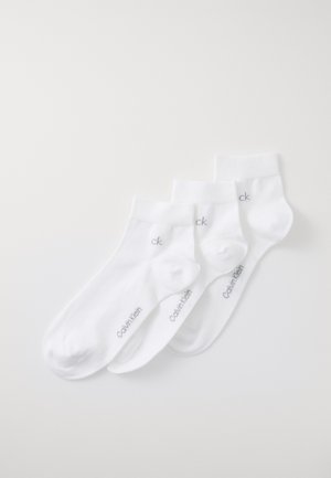 Tři páry bílých bavlněných ponožek do kotníku, s ribbenovým lemem a šedým logem "Calvin Klein" na boku. Měkká textura a bezešvé špičky.