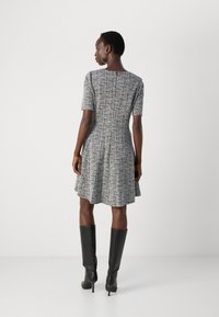 Mustakuvioinen tweed-mekko, jossa on lyhyet hihat ja leveä helma, tekstuuripinta ja pyöreä kaula-aukko, yhdistettynä polveen saakka ylettyviin mustiin saappaisiin.