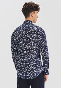 Granatowa koszula z długim rękawem w kwiatowy wzór z białymi kwiatami i zielonymi łodygami. Slim-fit z klasycznym kołnierzykiem i zapięciem na guziki.