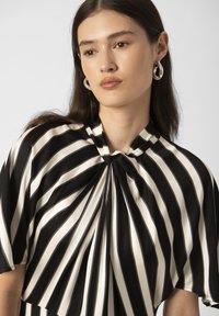 Black and white striped blouse with a knotted collar, short sleeves, and a soft, flowing texture. Features vertical and horizontal stripes.
