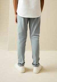 Pantalones tapered de color gris claro, hechos de una tela suave, con puños enrollados y combinados con zapatillas blancas, vistos desde la parte trasera.