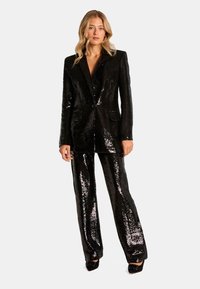 Costume noir en sequins avec une veste ajustée dotée d'un bouton unique, de revers en notch et de pantalons à jambes droites. Le tissu texturé et brillant accentue l'éclat.
