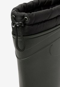 Green rubber boot with a black fabric cuff and drawstring. Textured surface with a smooth finish. Features a logo detail on the side.