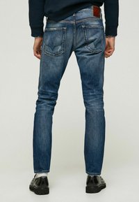Jean en denim bleu foncé avec une coupe droite, dotés de deux poches arrière, d'un léger délavage et d'une étiquette en cuir au niveau de la taille.