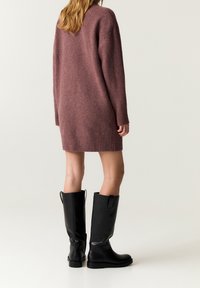Robe-pull en maille oversize rose pâle avec poignets et ourlet côtelés ; portée avec de hautes bottes en cuir noir dotées d'onglets de traction.