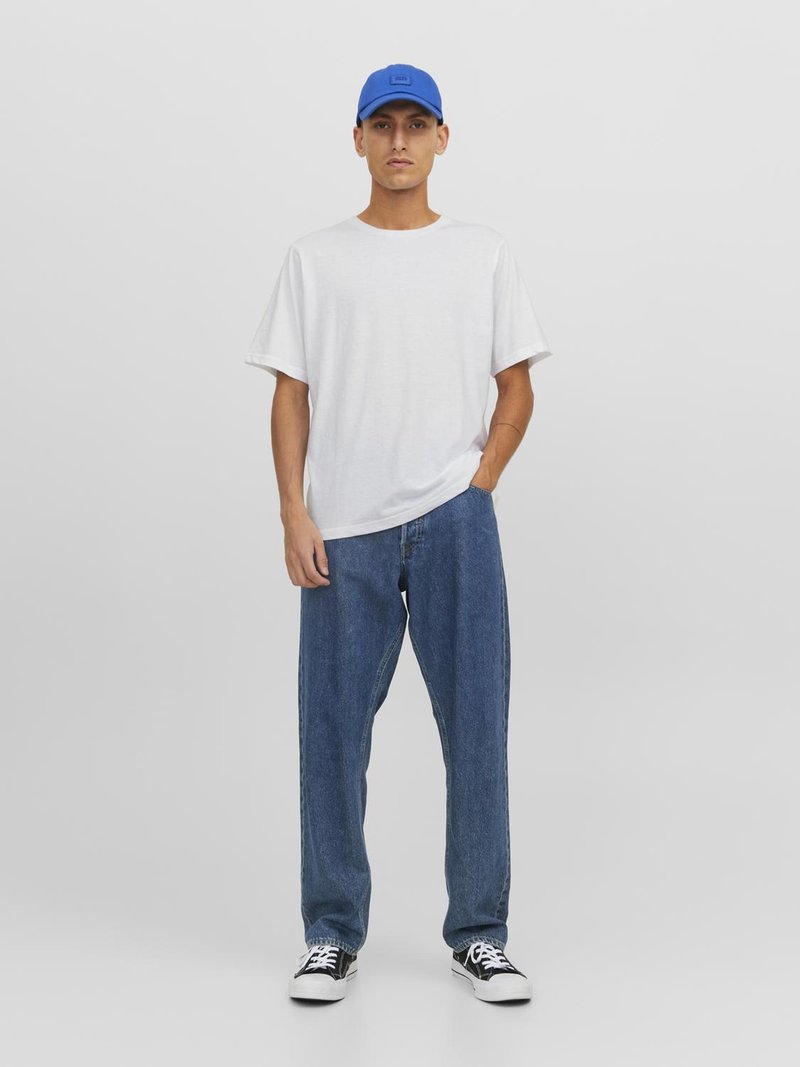T-shirt en coton blanc, ample, associé à un jean en denim bleu. Baskets noires et blanches, accentuées d'une casquette bleue. Fond uni.