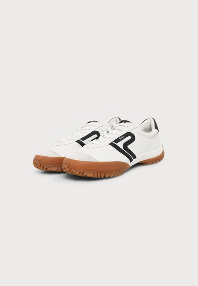 Λευκά sneakers χαμηλού προφίλ με μαύρες πλευρικές ρίγες, καφέ υφασμένους πάτους, λευκά κορδόνια και επενδεδυμένα πέτα, σε απλό φωτεινό φόντο.