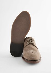 Suède dresschoenen in lichtbruin, met vetersluiting, geperforeerde details op de neus en een gestructureerde rubberen zool. Lage hak.