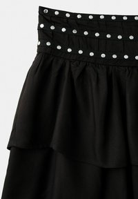 Jupe noire à plusieurs couches avec une taille large présentant trois rangées de clous argentés en lignes horizontales.