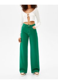 Gröna vida byxor i denim med hög midja, framfickor och kontrasterande sömmar. Bärs med en vit långärmad topp.