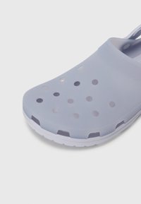 Light blue clogs made of flexible material featuring ventilation holes, textured surface, and a white outsole. Simple, rounded design.