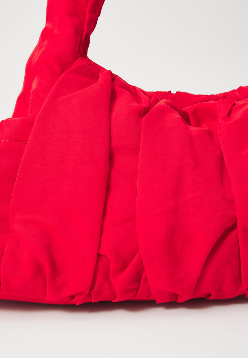Bolso de tela roja con un diseño de plisado texturizado, material suave y un asa resistente. El color es vibrante y no tiene herrajes visibles.