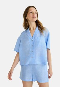 Chemise légère en lin bleu clair à manches courtes avec une poche et une patte de boutonnage, associée à un short assorti, présentant une coupe décontractée et une texture lisse.