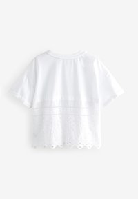 Witte korte mouw t-shirt met een kanten onderste helft met een golvende rand en bloemrijke borduursels. Zacht katoenen materiaal, losse pasvorm.